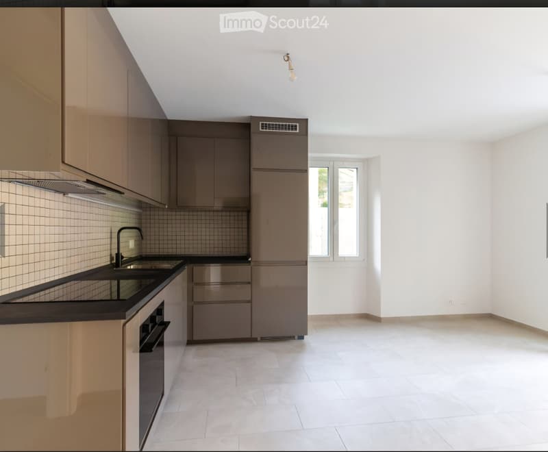 Modern kitchen with light-colored cabinets, a black countertop, and a stainless steel oven. The space is bright with white walls and tiled flooring.