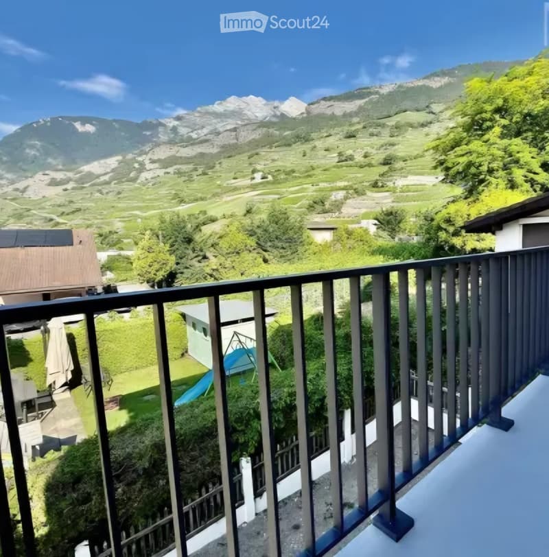 Balcony overlooking a scenic mountain landscape with green fields and scattered buildings below.