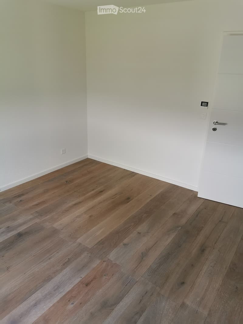 Empty room with light-colored walls and wooden flooring, featuring a white door and electrical outlets.