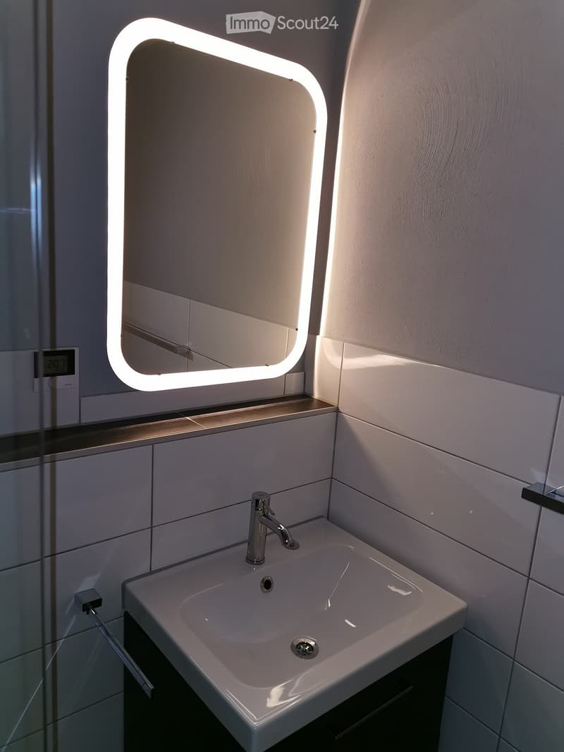Modern bathroom with a white sink, chrome faucet, and illuminated mirror with a sleek, curved design.