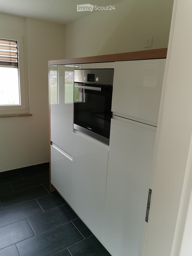 Modern kitchen with white cabinets, a built-in oven, and dark tiled flooring.