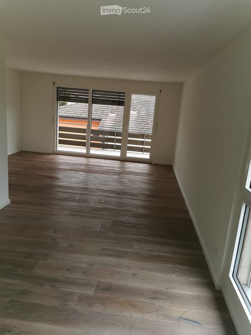 Empty room with wooden flooring, large sliding glass doors leading to a balcony, and white walls.