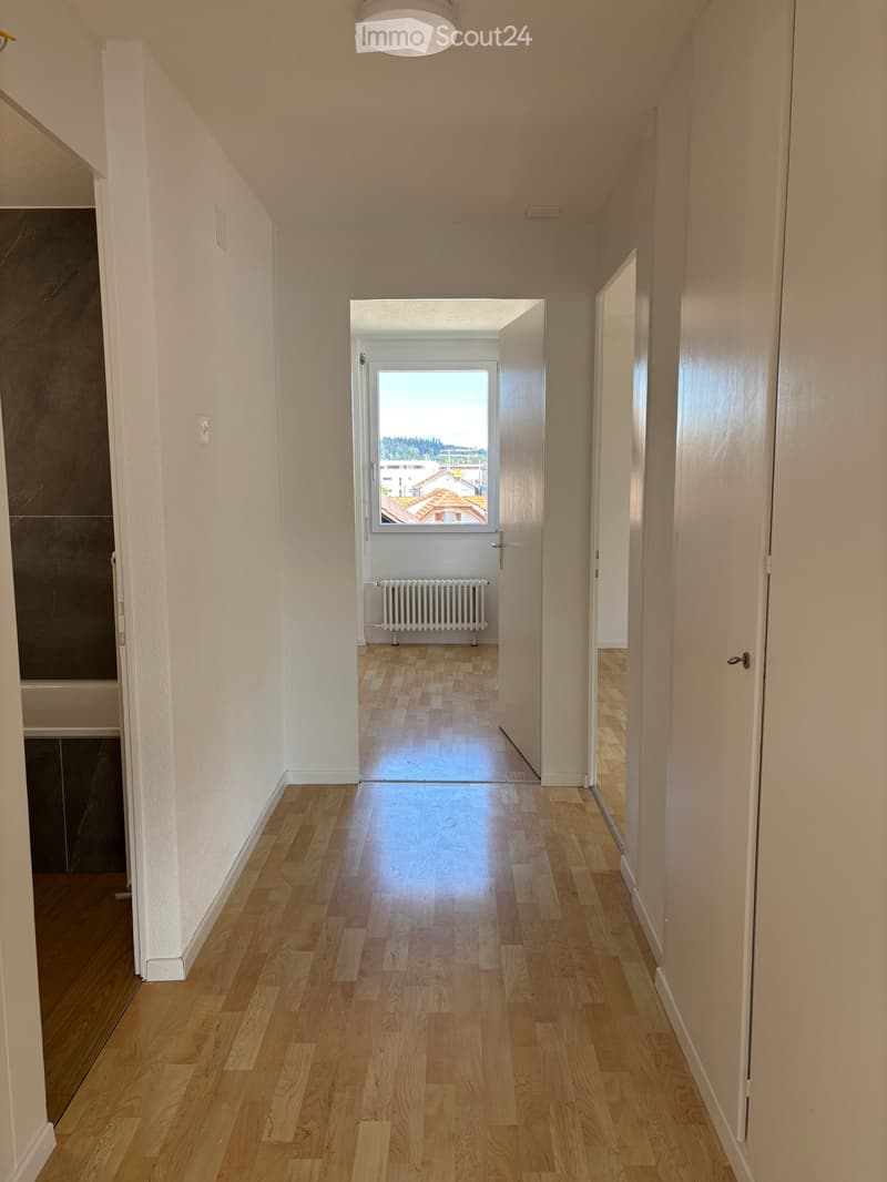 Empty hallway with hardwood floors, white walls, large window with view, white radiator