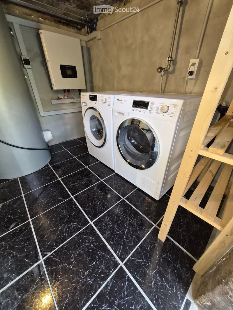 A bathroom with black marble flooring, white washing machine and dishwasher, and a control panel on the wall.