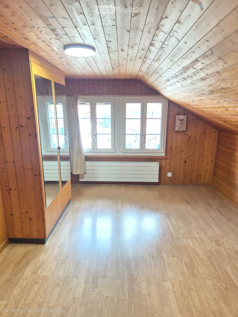 Empty attic room with wooden walls, ceiling, and floor, large windows, and a built-in wardrobe.