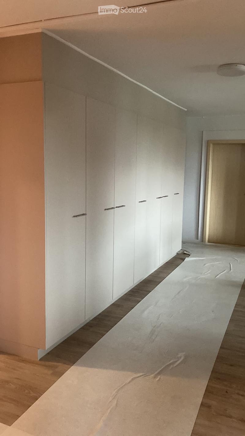 Modern hallway with white built-in cabinets, sleek black handles, and a polished concrete floor transitioning to wooden flooring.