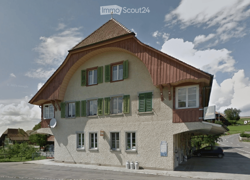 Traditional Swiss-style building with a pitched roof, green shutters, and a covered garage entrance.