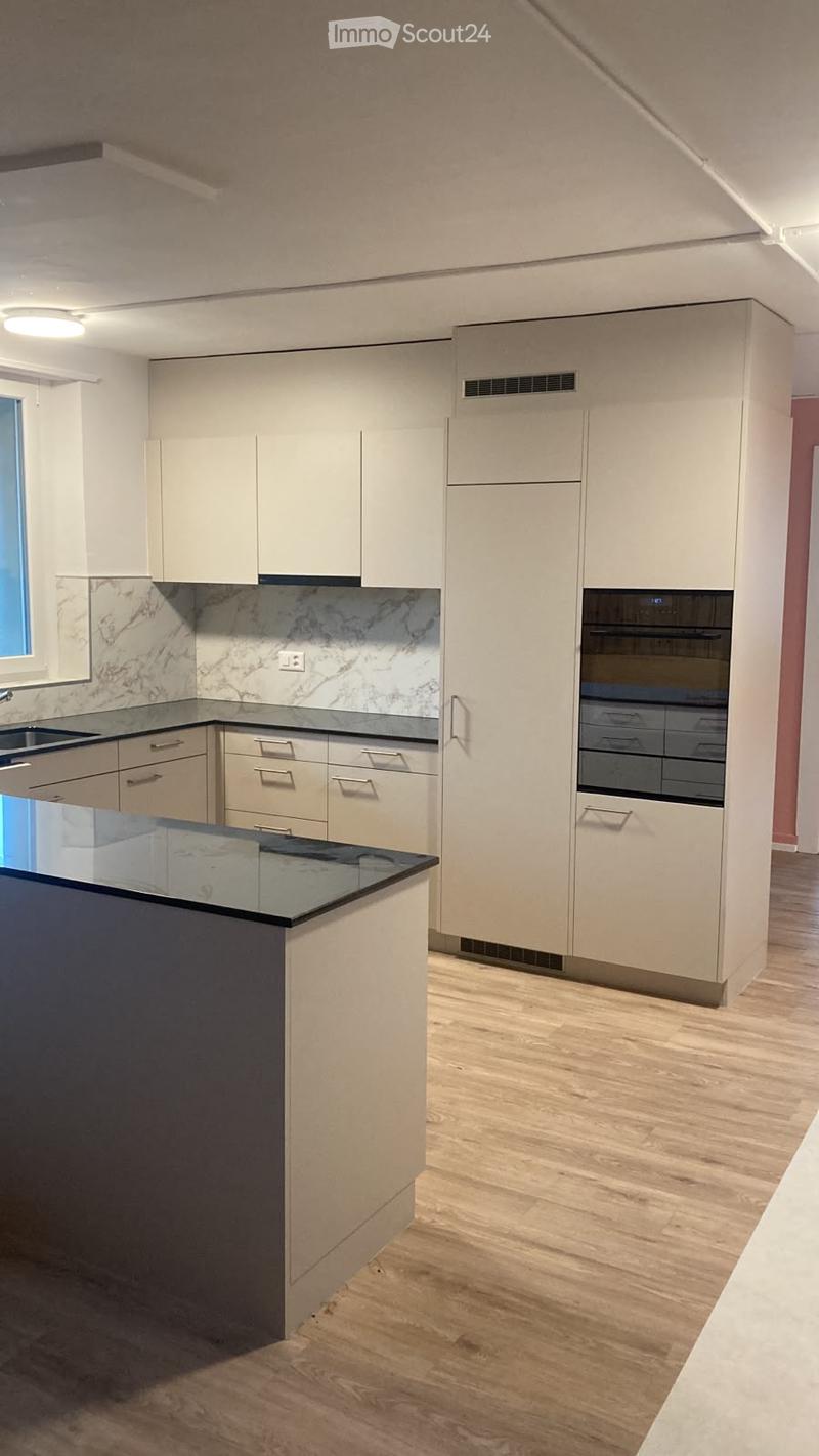Modern kitchen with light-colored cabinets, a central island with a black countertop, and a marble backsplash.