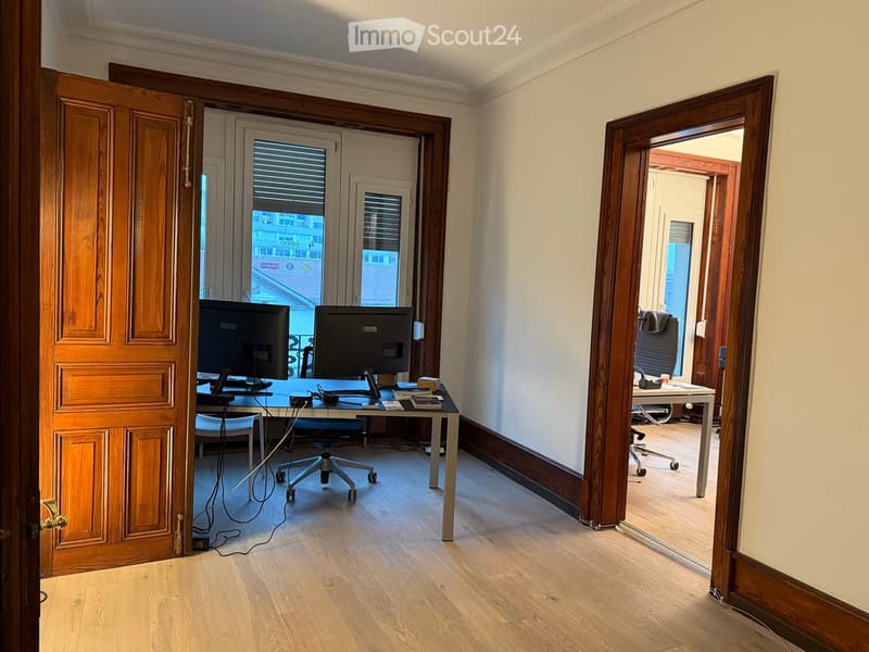 Office space with wooden flooring, two desks, chairs, and computer screens.