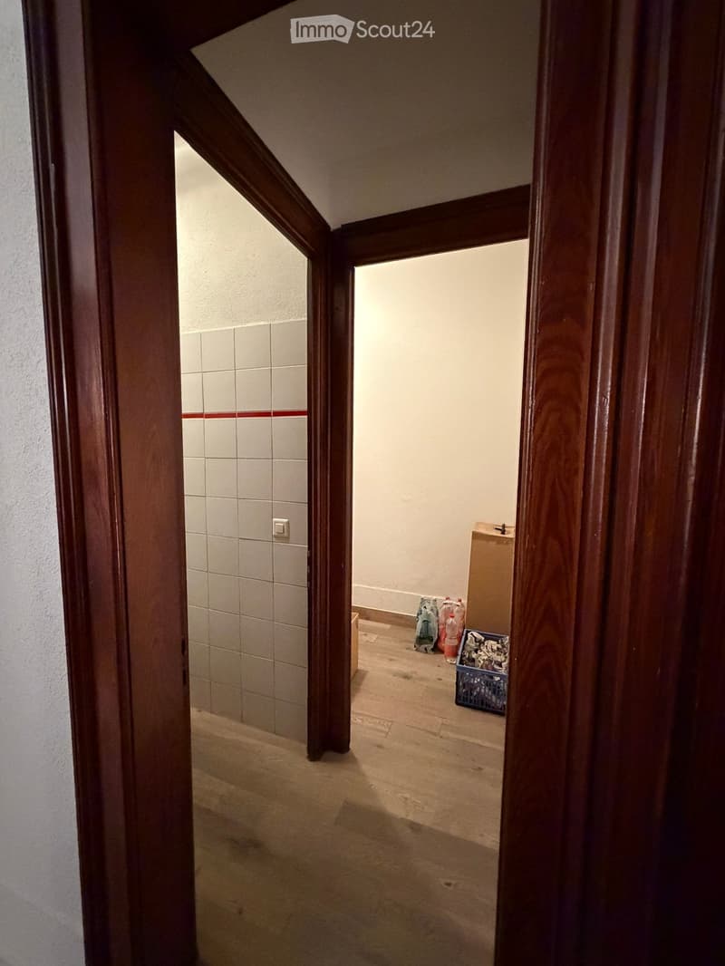Empty hallway with wooden doors, tiled wall, and light-colored floor. No furniture or items visible.
