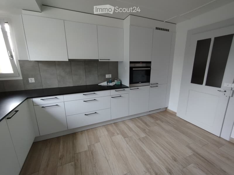 Modern kitchen with white cabinets, black countertop, and wooden flooring.