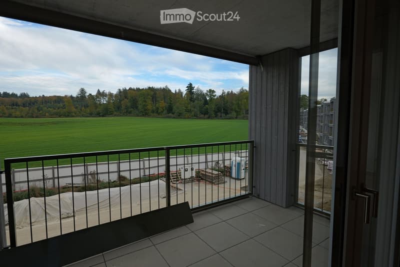 Balcony with tiled floor, metal railing, and a view of a green field and trees.