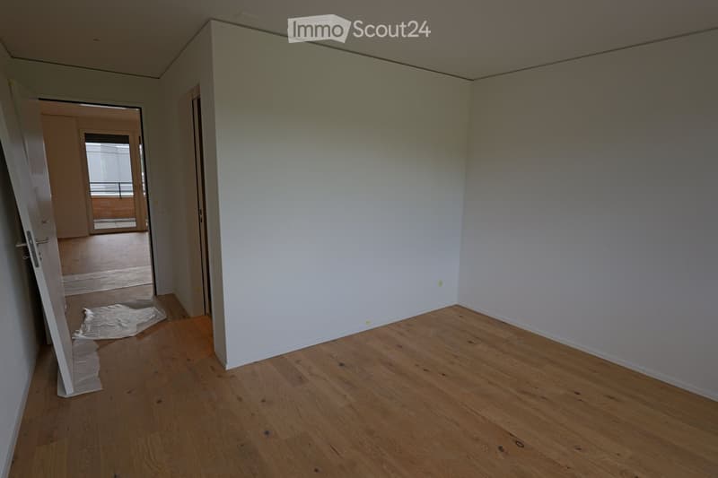 Empty room with wooden flooring and white walls, featuring an open doorway leading to another room with a balcony view.