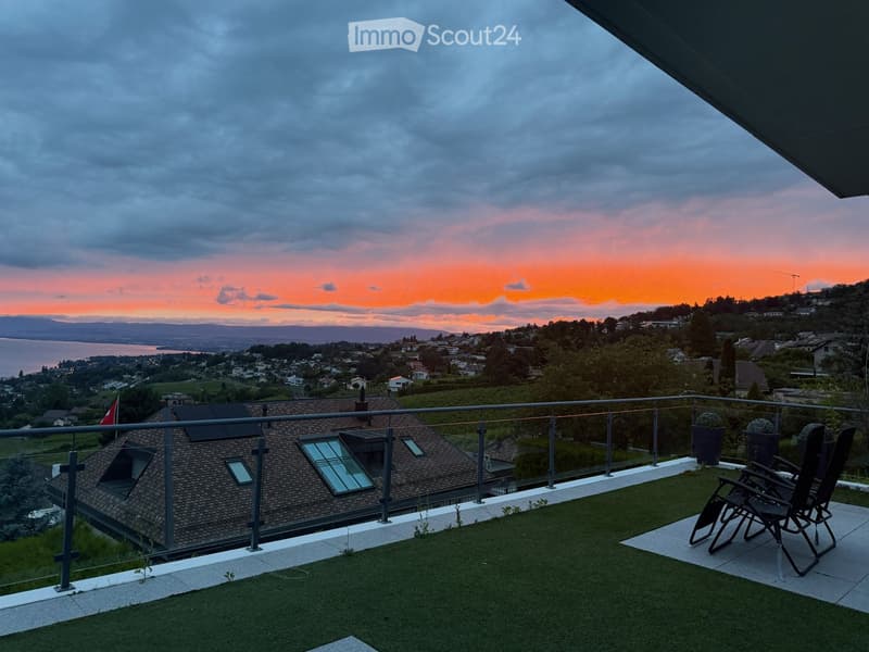 Balcony with artificial grass, two black chairs, and a view of a cityscape and lake at sunset.