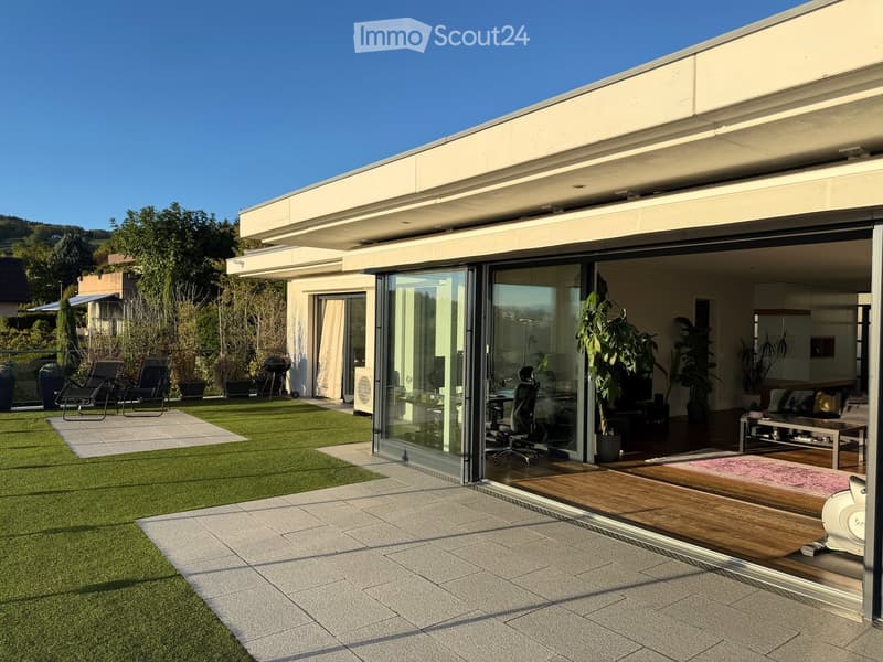 Modern outdoor space with artificial grass, patio tiles, lounge chairs, and a view of the surrounding landscape.
