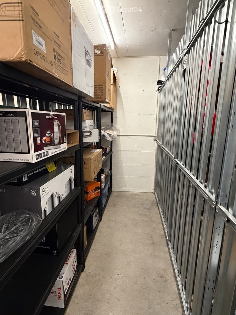 Empty hallway with metal shelving on one side holding various boxes and items, and metal framing on the other side.