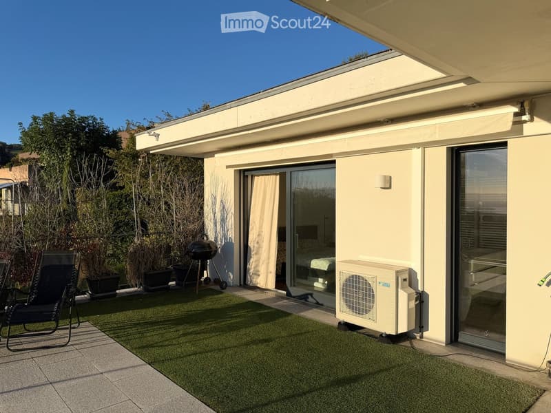 Balcony with artificial grass, a black folding chair, a grill, and an air conditioner unit.