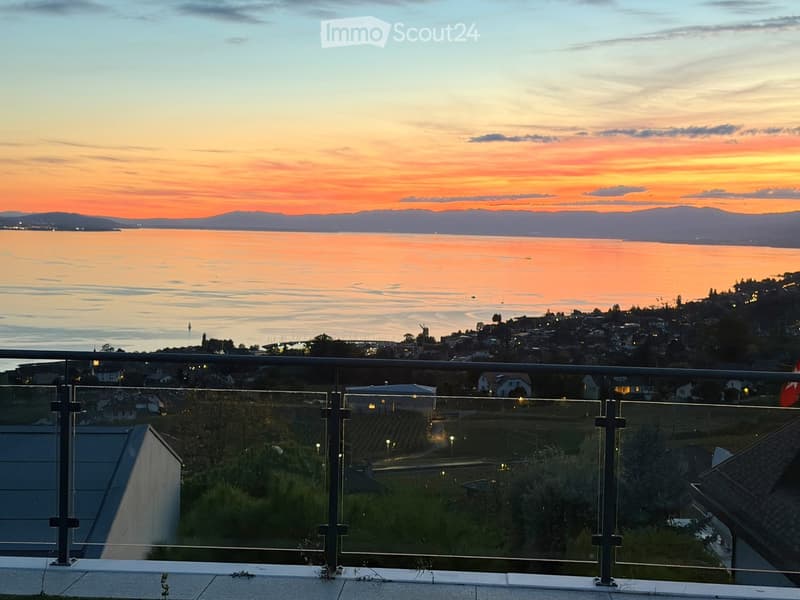 Balcony with glass railing overlooking a scenic view of a body of water, distant cityscape, and sunset sky.