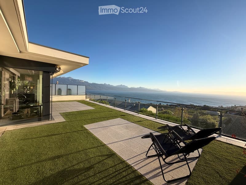 Modern rooftop terrace with artificial grass, sun loungers, and a panoramic view of the sea and mountains.
