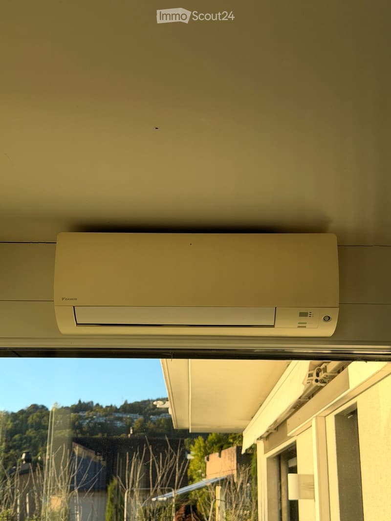 Balcony with a Daikin air conditioning unit mounted on the wall, overlooking a scenic view of a hillside with trees and buildings.