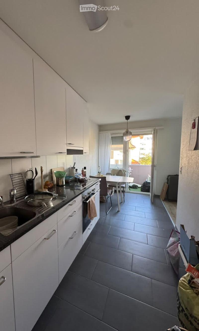 Modern kitchen with white cabinets, dark countertops, and stainless steel appliances. Includes a sink, stove, oven, and a dining area with a table and chairs.