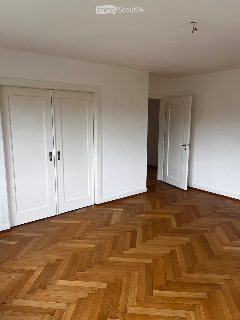 Empty room with wooden herringbone flooring, white walls, and white doors.
