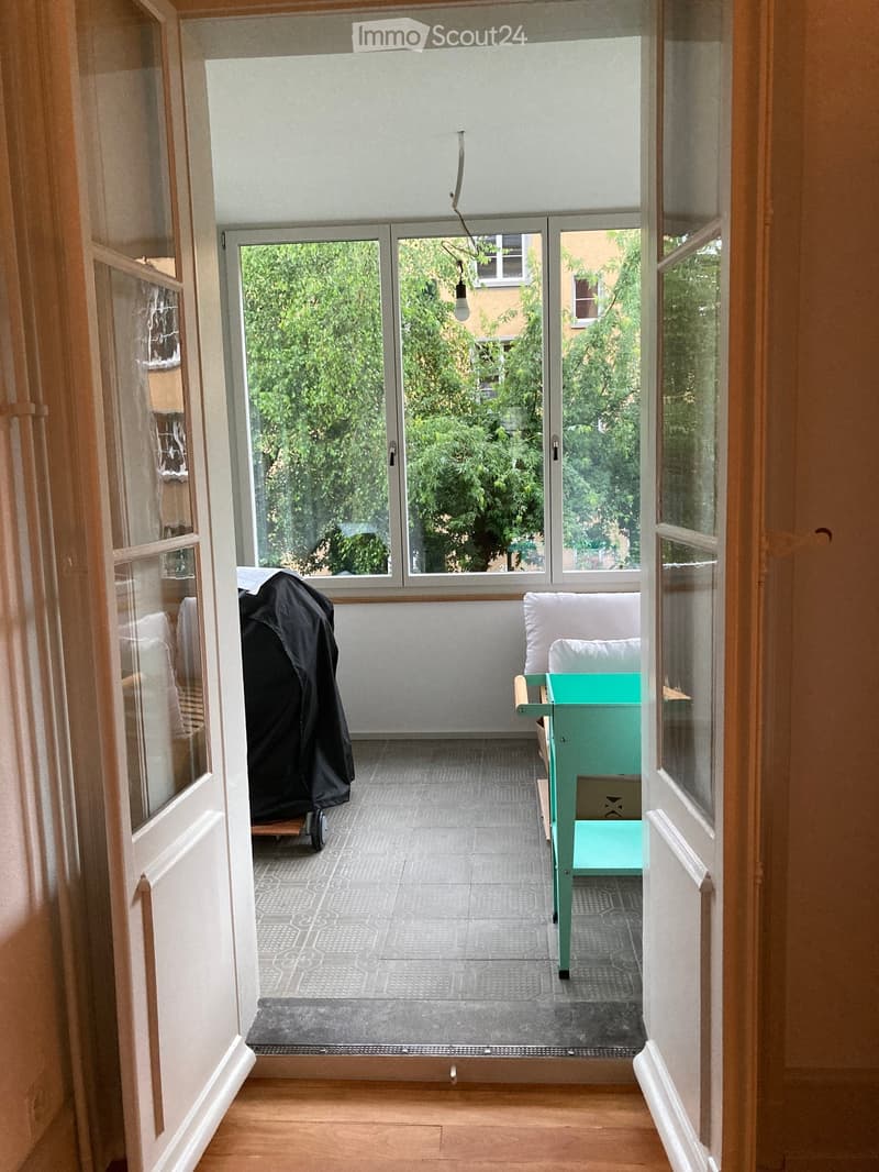 Balcony with grey tiled floor, large glass doors, green chair, and small table.