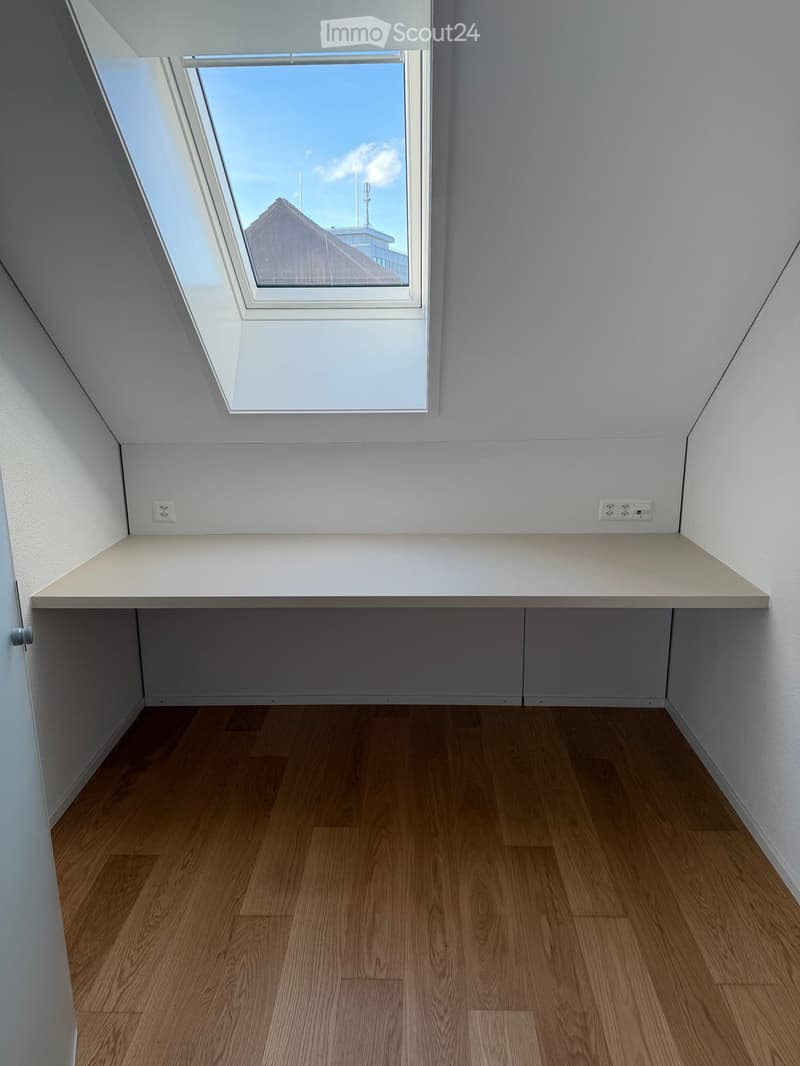 Empty room with wooden flooring, white walls, and a built-in shelf beneath a skylight window.