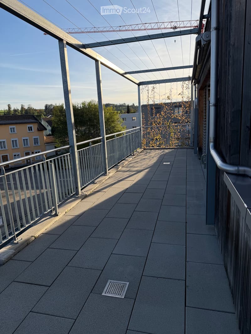 Balcony with tiled floor, metal railing, and a view of the surrounding area, including buildings and trees.