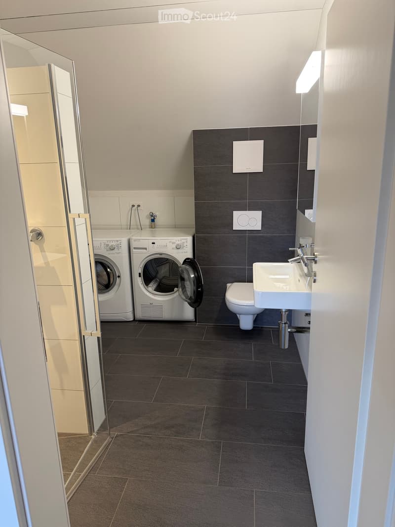 Modern bathroom with dark tiled floor, white sink, toilet, and two white washing machines/dryers.