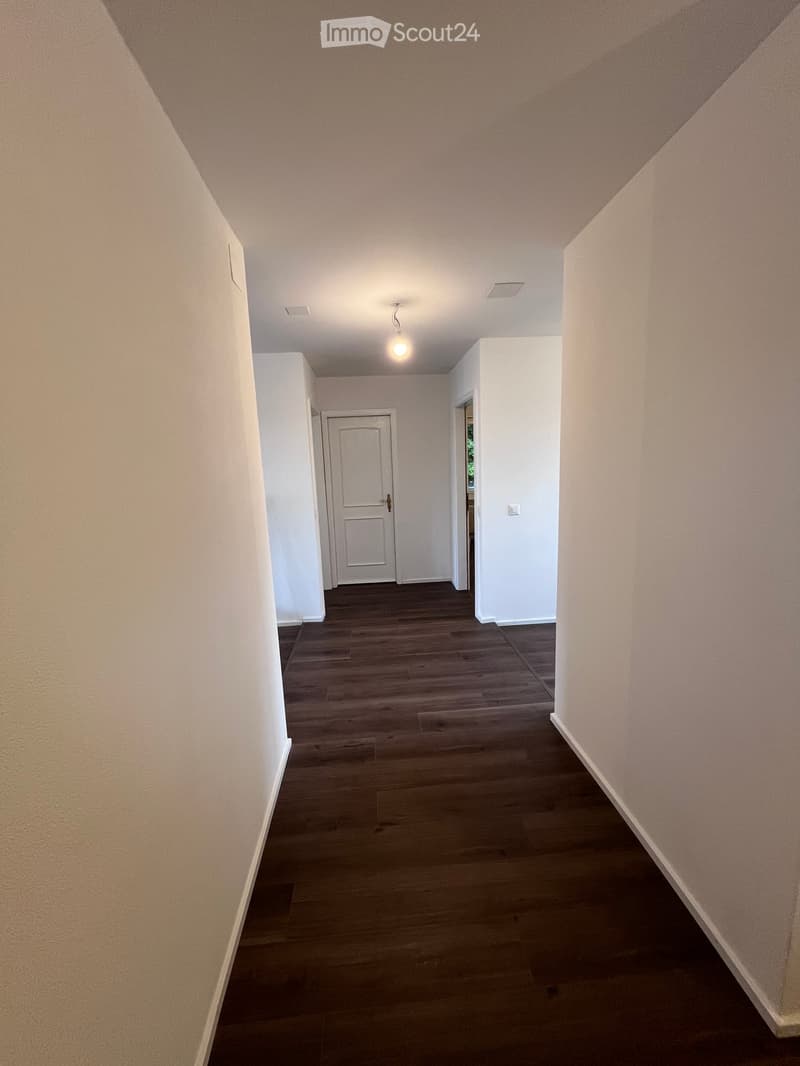 Empty hallway with wooden flooring, white walls, and a single door at the end.