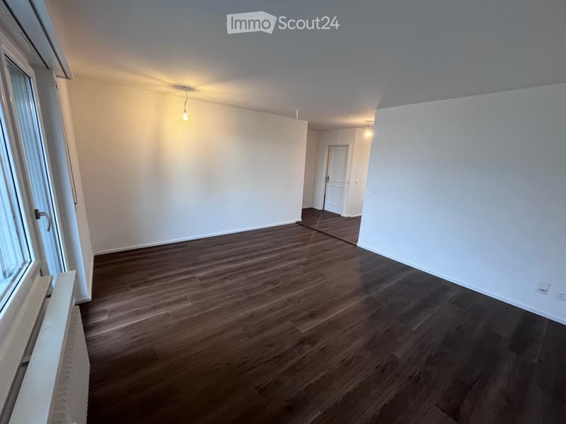 Empty room with wooden flooring, white walls, and a single door leading to another space.