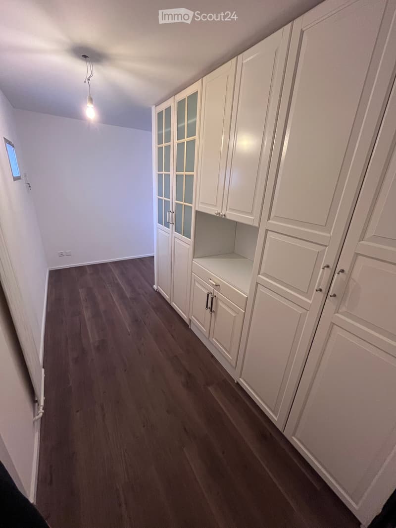 Empty room with white walls, dark wooden flooring, and built-in white cabinets with glass doors and drawers.
