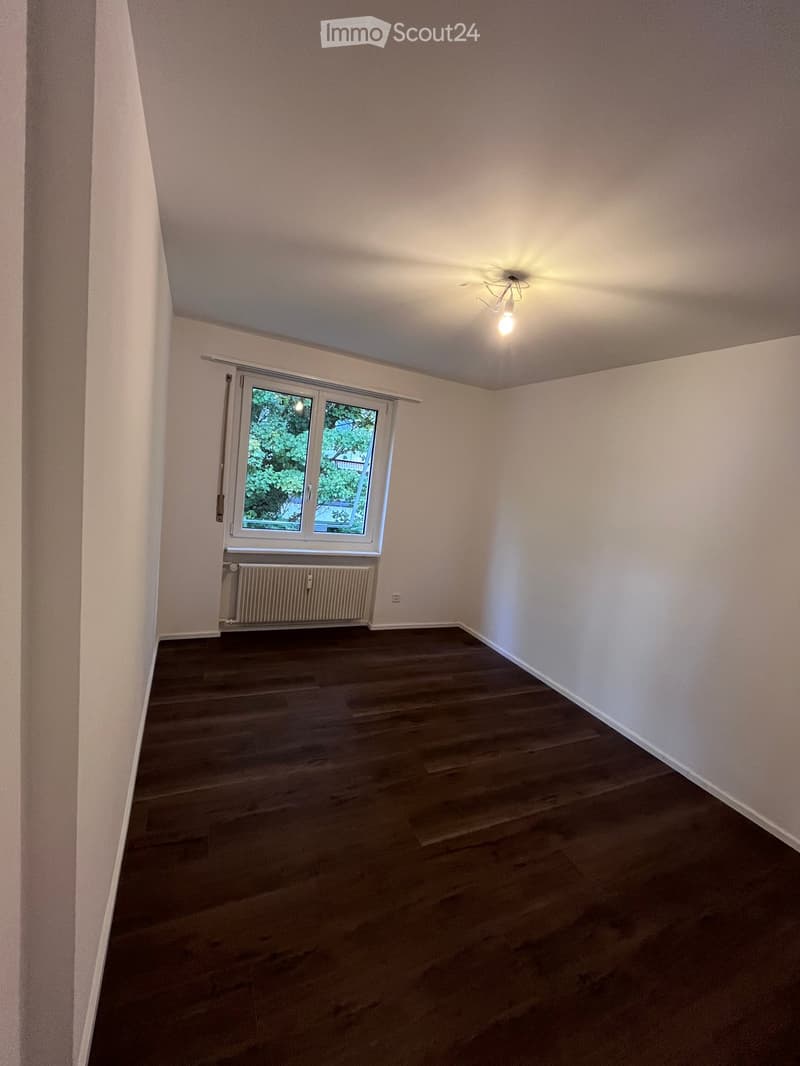 Empty room with wooden flooring, white walls, a window with blinds, and a radiator below it.