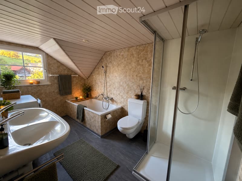 Modern bathroom with a large window, a double sink, a bathtub, a toilet, a walk-in shower, and decorative towels and candles.