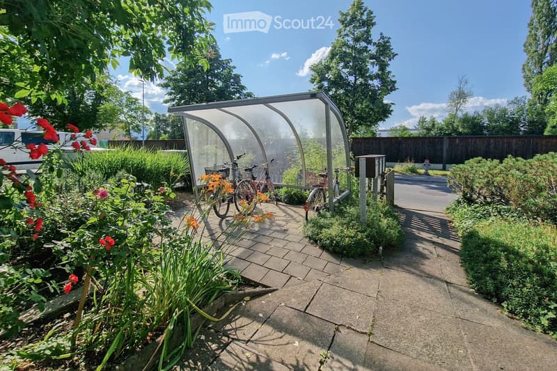 Garden area with paved walkway, bicycle shelter, flowers, and greenery.