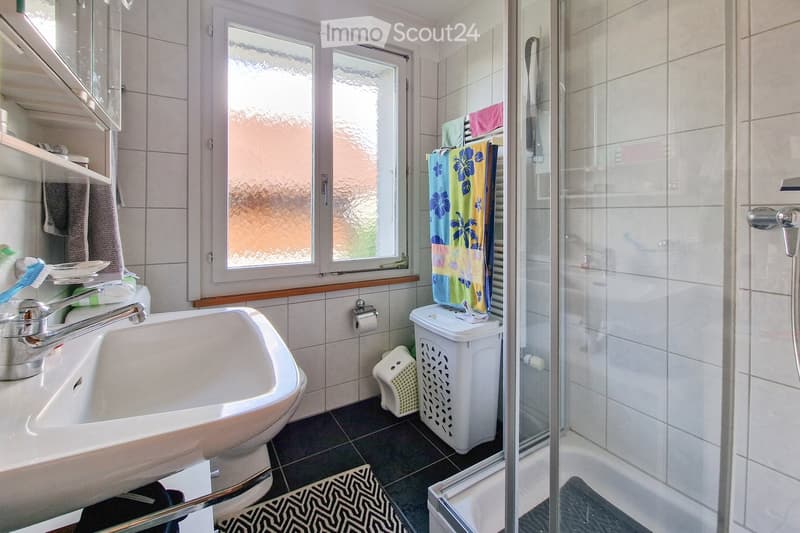 Bathroom with a sink, faucet, toothbrush, toilet paper, towels, a shower, laundry basket, and a rug.