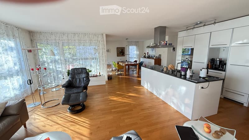 Open-plan living and dining area with a modern kitchen. Features a sofa, coffee table, dining table with chairs, kitchen island, and various appliances.
