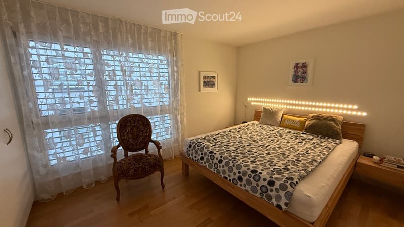 Cozy bedroom with a wooden bed, patterned bedspread, decorative chair, nightstand, and framed artwork on the wall.