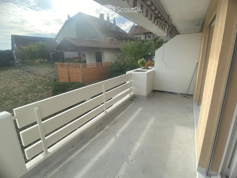 Balcony with white railing, concrete floor, and a small white planter. The view shows a fenced yard with trees and neighboring houses.