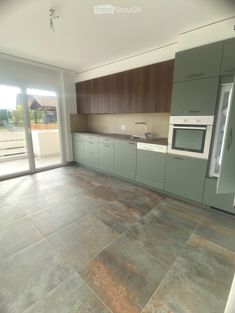 Modern kitchen with grey and brown cabinets, stainless steel appliances, and a large window offering a view of the outdoor area.
