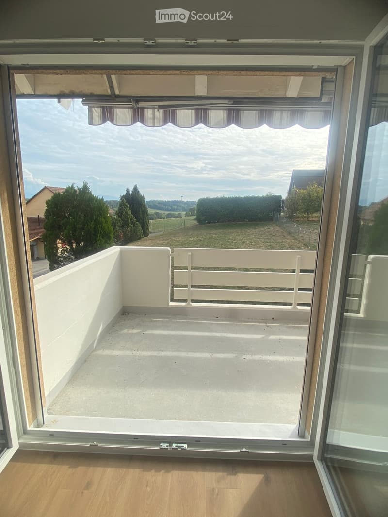 Balcony with white railing, overlooking a green landscape with trees and houses.