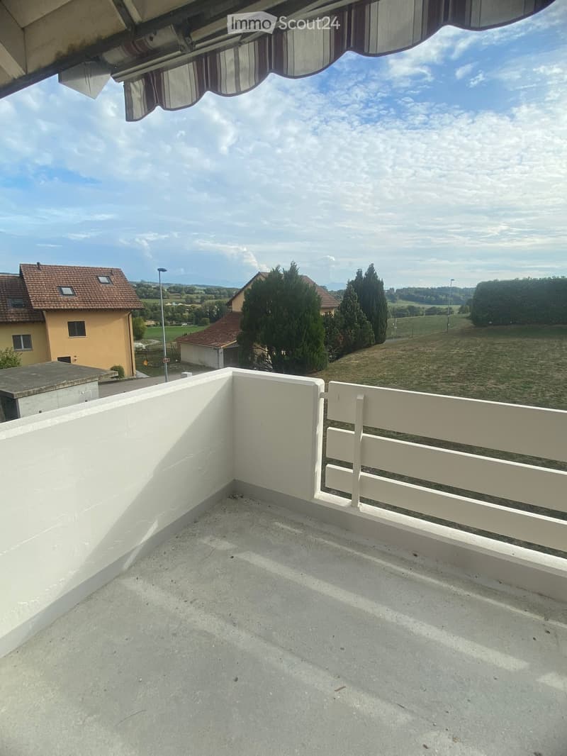 Empty balcony with white railing, concrete floor, and scenic countryside view.