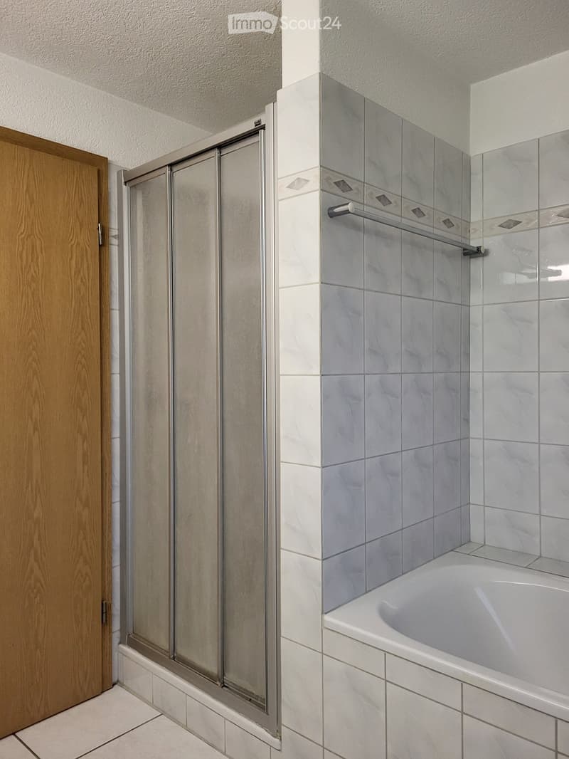 Modern bathroom with a bathtub, glass shower stall, and a wooden door.