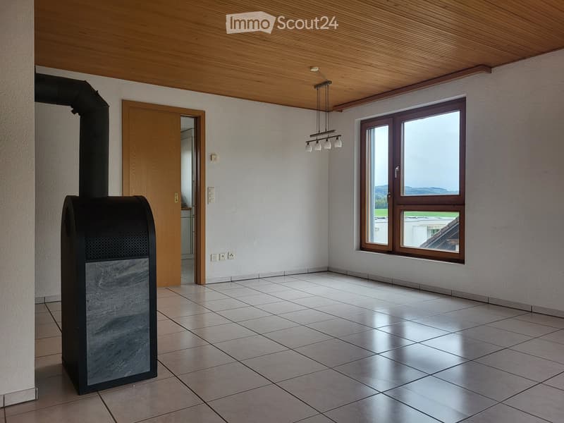 Empty room with tiled floor, white walls, wooden ceiling, large window, and a black wood-burning stove.