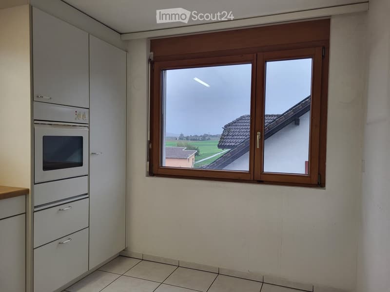 Modern kitchen with white cabinets, built-in oven, and a large window overlooking a rural landscape.