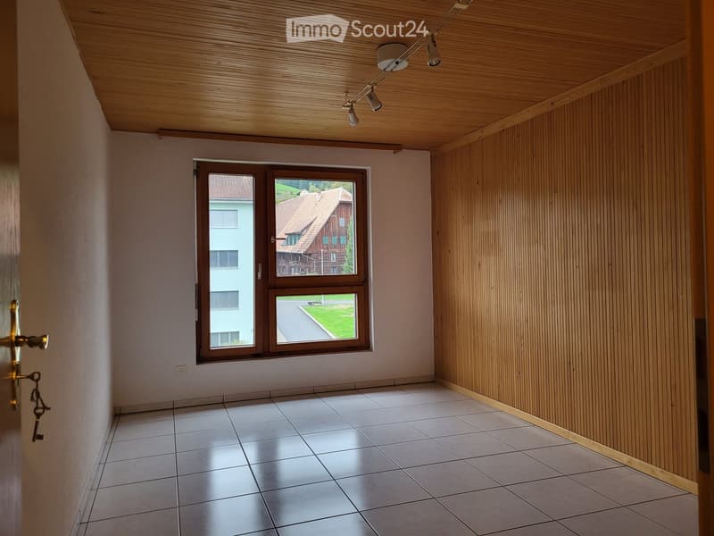Empty hallway with wooden panel walls, tiled floor, and large window showing a view of the street and neighboring houses.