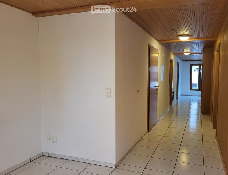 Clean hallway with tiled floor, white and beige walls, wooden doors, and recessed lighting.