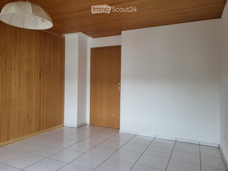 Empty room with tiled floor, white walls, wooden ceiling, and a single wooden door.