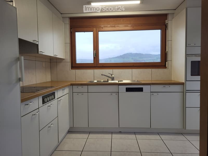 Modern kitchen with white cabinets, wooden countertops, and a large window overlooking a scenic view.